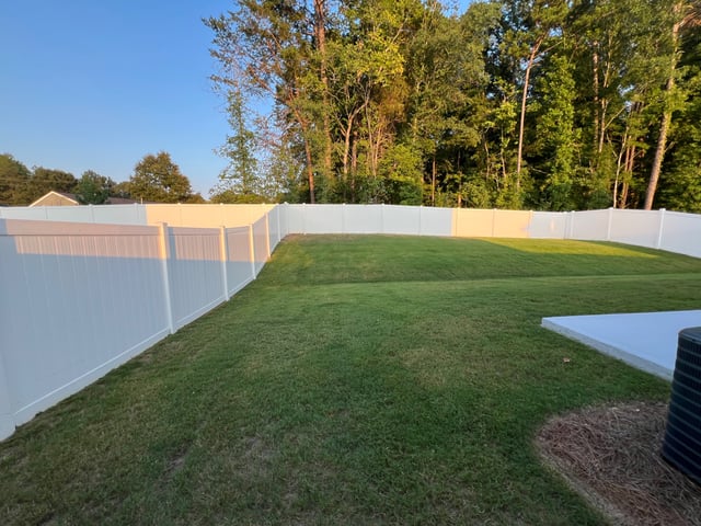 Mowed backyard lawn inside a white privacy fence