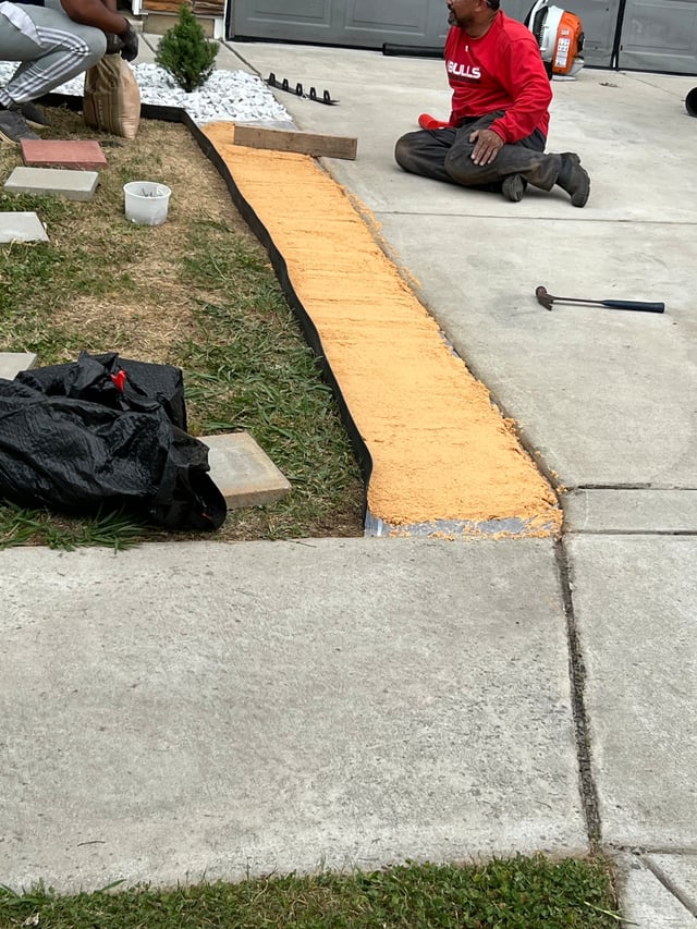 Sand base laid for a new paver border beside a driveway